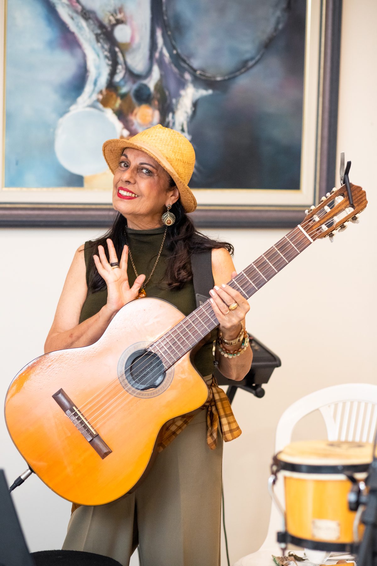 Retrato de Waleska Santos de chapéu de palha, segurando o violão e sorrindo